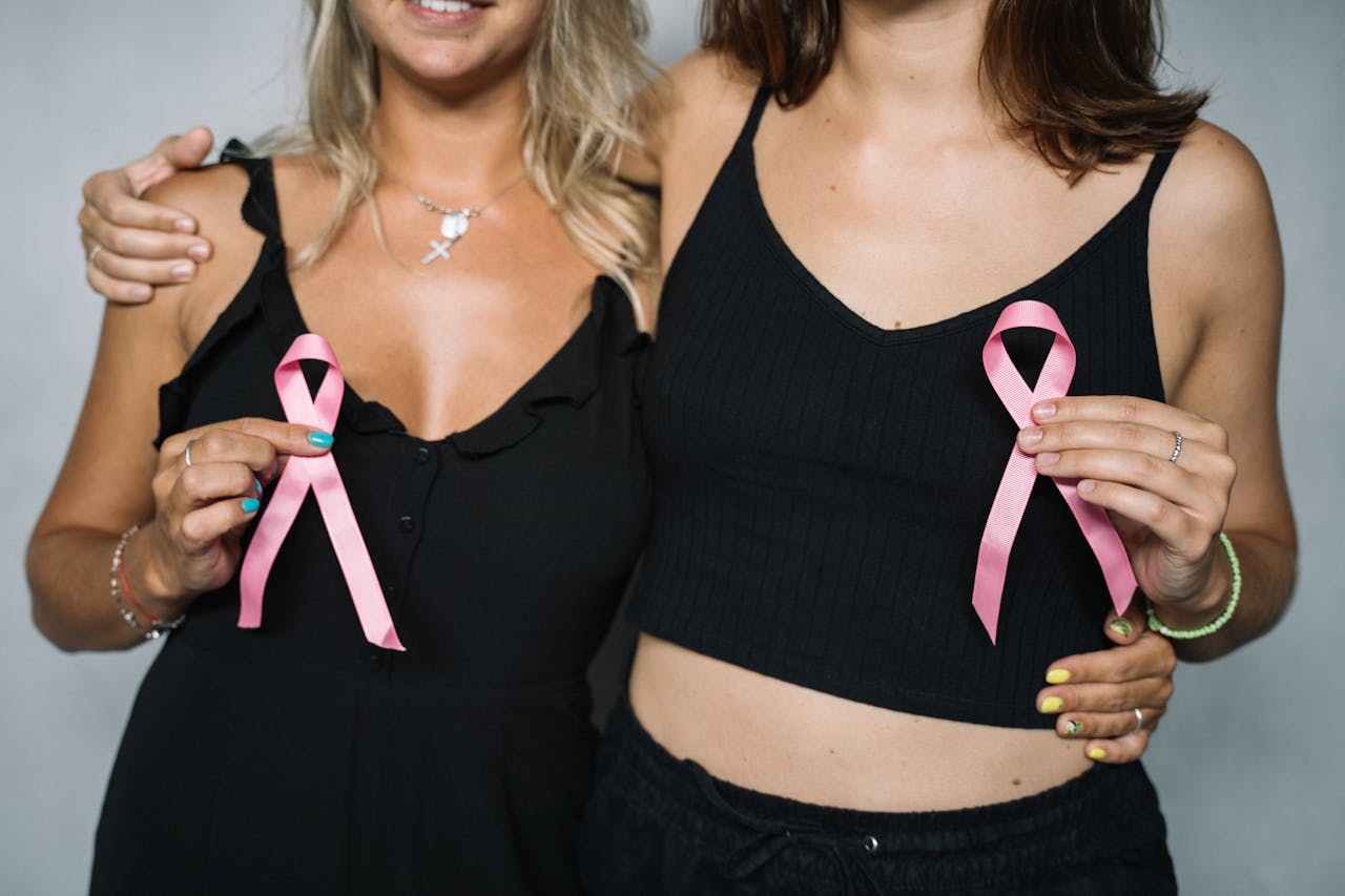 services-03 Two women showing support for breast cancer awareness by holding pink ribbons.