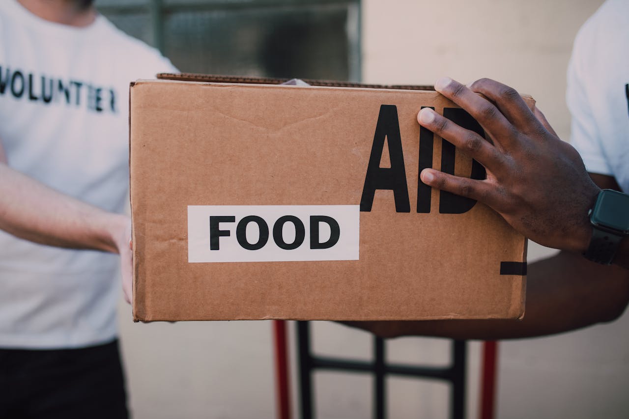 why-choose-us Two volunteers handing over a box labeled 'Food Aid', symbolizing community support.